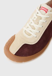 Sneakers din suede bej și burgund cu talpă din cauciuc, șireturi plate albe și etichetă roșie cu logo-ul "Camper" pe limbă. Vârf rotunjit, texturat.
