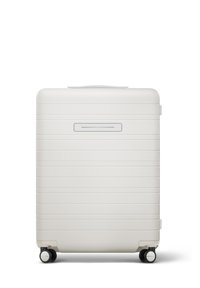 Valise rigide blanche avec des rainures horizontales, une poignée supérieure, un compartiment pour ID slim, et quatre roues noires pour la mobilité.
