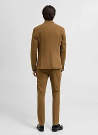 Brown tailored suit with a single vent, straight-cut trousers, and minimalist design, complemented by black shoes.