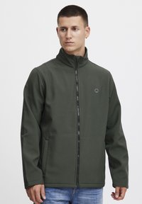 Dark green zip-up jacket with a high collar, made from a smooth, sturdy fabric. Features side pockets and a small logo on the chest.