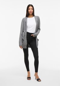 Gray cardigan made of soft knit fabric, open front, long sleeves with ribbed cuffs, paired with black skinny jeans and black heeled sandals.