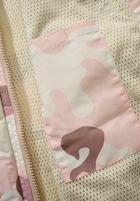 Lätt mesh-tyg i krämfärg med en rosa kamouflageficka; har en dragkedja och en texturerad yta.