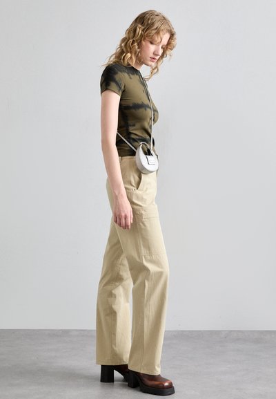 Green tie-dye fitted t-shirt, beige wide-leg trousers, brown platform ankle boots, and a small silver crossbody bag. Minimalist design.