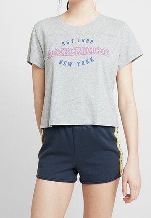 T-shirt grigia corta con stampa rosa e blu "Abercrombie New York", abbinata a pantaloni corti navy con strisce gialle laterali.