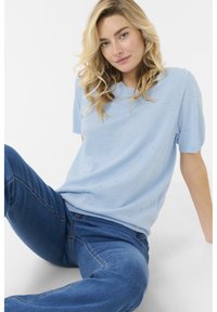 Pull léger bleu à manches courtes avec un motif en relief. Tissu tricoté doux avec un col rond, associé à un jean en denim bleu.