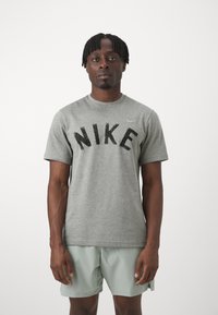 Pelēka kokvilnas T-kreklu ar melnu "NIKE" logo treknā burtu stilā, apaļo kakla izgriezumu un īsām piedurknēm, kopā ar gaiši zaļām šortiem.