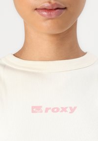 T-shirt blanc côtelé avec un logo "roxy" rose sur le devant, encolure ronde et texture douce.