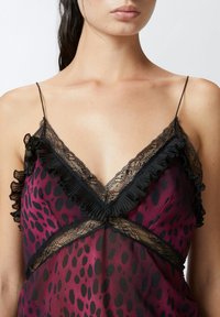 Top s čipkastim rubom i dubokim V-izrezom, s volanima, u burgundi boji s crnim leopardskim točkicama na prozirnom materijalu. Uključene su podesive naramenice.