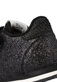 Sneaker nera con una parte superiore testurizzata e glitterata, dotata di un accento intrecciato nero sul tallone e di una suola in gomma bianca.