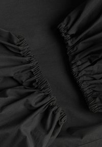 Tissu noir avec bords élastiqués et froncés, probablement une partie d’un drap-housse ou d’un vêtement, gros plan montrant la texture et les détails des coutures.