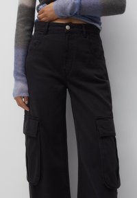 Zwarte cargobroek van katoen, met zijzakken, een knoopsluiting en een losse pasvorm, gecombineerd met een kleurrijke gebreide trui.