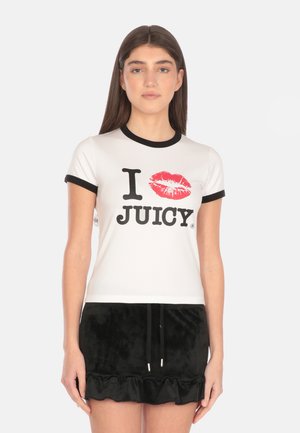 T-shirt bianca in cotone con collo a contrasto nero, caratterizzata da una stampa di labbra rosse e testo nero in grassetto che recita "I JUICY." Il modello indossa una gonna nera a balze.