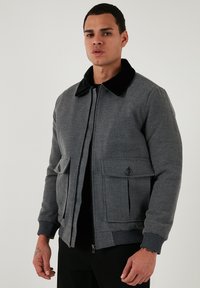 Sivá bomber bunda s čiernym kožúškom, so zapínaním na zips, manžetami s rebrovaním a dvoma prednými vreckami s gombíkovými detailmi.