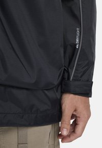 Black waterproof jacket featuring a textured fabric, with a fitted cuff and a reflective stripe along the sleeve. Branding visible on the shoulder.
