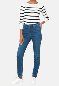 Striped white and navy long-sleeve top paired with fitted blue denim jeans and white sneakers. Simple design, clean lines, and casual style.