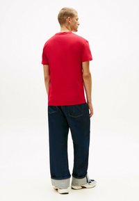 T-shirt rosso a maniche corte con taglio dritto, abbinato a jeans in denim blu a vestibilità comoda con risvolti e una texture leggermente sbiadita.