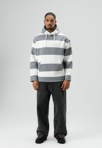 Grijs-witte gestreepte hoodie met een zak aan de voorkant, trekkoorden, lange mouwen, gecombineerd met donkere spijkerbroek en zwarte veterschoenen.