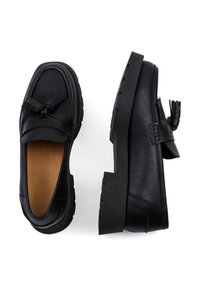 Black leather loafers with a braided tassel detail, flat rubber sole, rounded toe, and subtle textured finish.