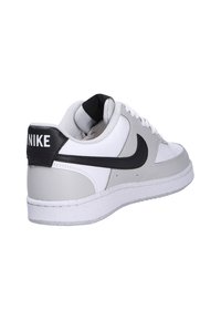 Nike sneaker with white leather and grey accents, featuring a black heel tab, round toe, and textured sole. Black swoosh logo on side.