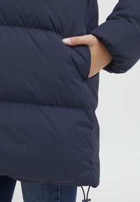 Navy puffer jacket featuring a quilted design, side pocket, and adjustable hem. Material appears smooth and water-resistant.