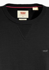 Pull en maille noire avec encolure côtelée et détail en point en V. Présente un petit logo Levi's noir en bas à droite. Étiquette taille M incluse.