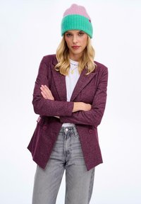 Burgundowy teksturowany marynarka z dwoma guzikami, w połączeniu z szarymi dżinsami. Całość dopełnia pastelowa różowa i zielona czapka.