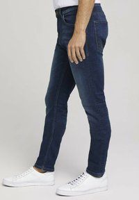 Jeans ajustados de color azul oscuro con un diseño clásico de cinco bolsillos, fabricados en denim, combinados con zapatillas bajas blancas.