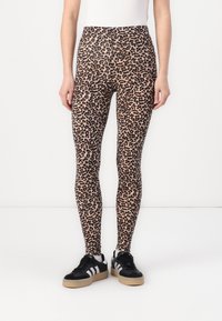 Lopende leggings met luipaardprint, gemaakt van elastisch materiaal, met een hoge tailleband en een aansluitende pasvorm. Gecombineerd met zwarte sneakers met beige zolen.