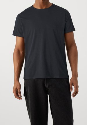 Musta crew-neck t-paita pehmeästä ja sileästä kankaasta, jossa on lyhyet hihat. Yhdistetty tummiin housuihin, luoden rentoa ilmettä.