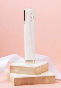 StylPRO skönhetsverktyg, vitt med texturerat grepp. Guldaccent vid basen, stående på vita och trähexagonala ytor mot en rosa bakgrund.