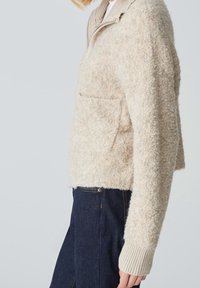 Cream-colored fuzzy sweater with a quarter-zip collar, ribbed cuffs, and a front pocket. Fabric has a soft, textured appearance.
