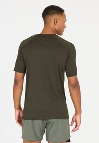 Kurzärmliges, tailliertes Sportshirt in Olivgrün, aus hochwertigem, feuchtigkeitsableitendem Gewebe. Verfügt über Raglanärmel und einen abgerundeten Saum.