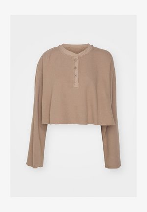 Kärbitud beež pikkade varrukatega topp, soonikkoes, ümmargune kaelus, nööpide rida, toores serv ja vabalt lendav lõige.