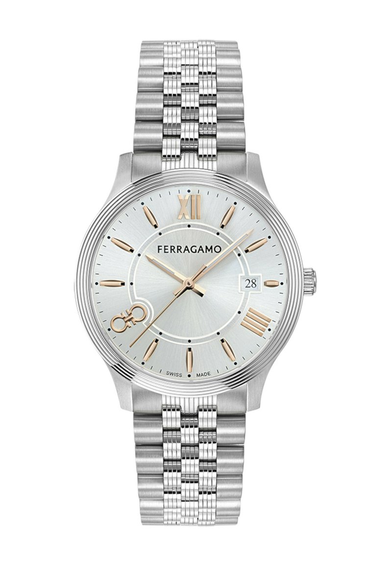 Hõbedane roostevabast terasest kell hõbedase diali, kuldsete akcentide, rooma numbrite markerite ja tekstureeritud käeverega. Omab kuupäeva kuvandit.