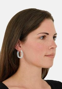 Zilveren hoepel oorbellen met gelaagd cirkelontwerp, met een gestructureerde afwerking en gladde randen, gedragen door een model met lang bruin haar.