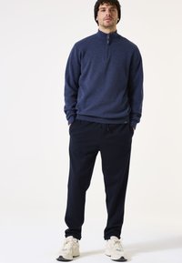 Marineblauwe fleece sweatshirt met rits tot halverwege, gecombineerd met marineblauwe joggingsbroeken met een zachte textuur en een elastische tailleband, afgewerkt met witte sneakers.