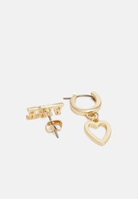 Brincos de ouro com um pendente em forma de coração em argola e um pírcing separado com a palavra "EASY" em letras recortadas. Textura metálica suave.