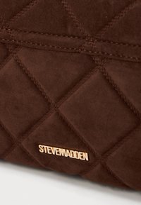 Brūnais kvilts audums ar zelta "STEVE MADDEN" logotipa aparatūru apakšā. Satur izšūtu dimantu rakstu un gludu tekstūru.