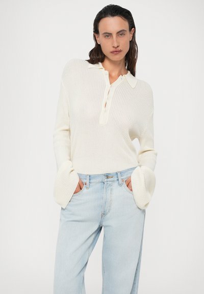 Maglione a coste color crema con colletto e bottoni. Vestibilità ampia con maniche svasate. Abbinato a jeans a gamba dritta di un blu chiaro.