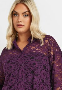 Purple lace blouse with floral pattern, button-down front, and soft texture. Features a collar and loose-fitting sleeves.