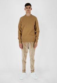 Maglione ribbed beige con scollatura rotonda, abbinato a pantaloni in corduroy beige e sneakers bianche, su uno sfondo neutro.
