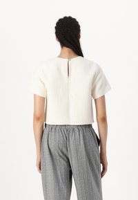 Short-sleeve, ivory textured top with a back keyhole opening, paired with gray patterned elastic-waist trousers.