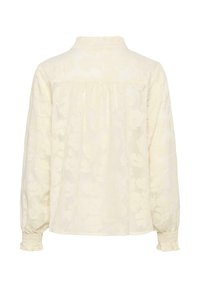 Blouse crème à manches longues avec motif jacquard floral, empiècement froncé au dos, col montant et poignets smockés avec bordure à volants.