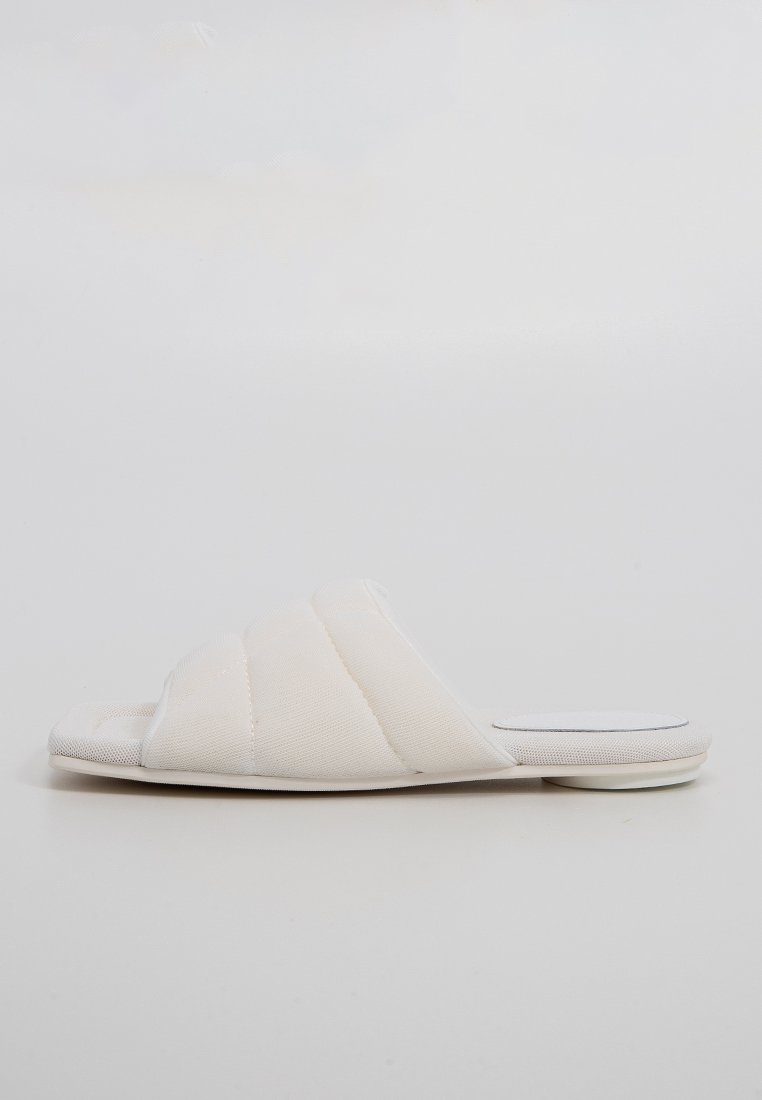 Sandales blanches à glisser avec une texture matelassée, un design à bout ouvert et une semelle en caoutchouc plate. Esthétique simple et minimaliste.