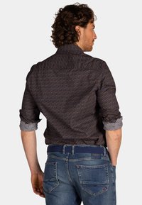 Donker gestippeld shirt met oranje en blauwe ontwerp, opgerolde mouwen met een lichter patroon, gecombineerd met blauwe jeans. Zichtbare riem.