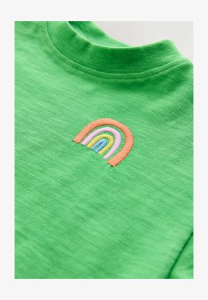 Zielona koszulka z krótkim rękawem z fakturowanej tkaniny. Na piersi znajduje się mały haftowany tęczowy detal w kolorach różowym, pomarańczowym i niebieskim.