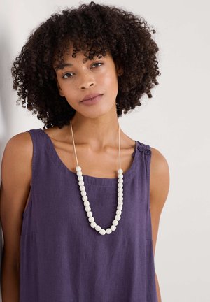 Lila Leinen-Tanktop mit rundem Halsausschnitt und einer seitlichen Tasche, ergänzt durch eine lange Halskette aus weißen Perlen.
