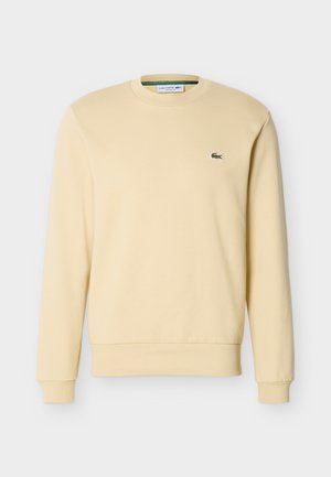 Felpa beige a maniche lunghe con scollo rotondo, polsini e orlo a coste, con un piccolo logo di un coccodrillo verde sul petto a sinistra.