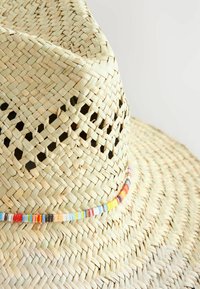 Sombrero de paja trenzada con ala ancha, que presenta una banda colorida de cuentas alrededor de la corona. Color beige claro con patrones de tejido intrincados.