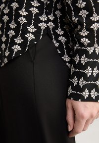 Black blouse with a white floral pattern, paired with black textured pants. The blouse features a curved hem and long sleeves.